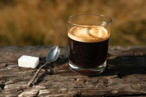 une tasse de café noir avec une petite cuillère et un sucre posés à côté
