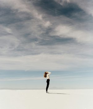 Une femme sur le sable blanc qui lève les yeux au ciel avec les mains sur ses yeux