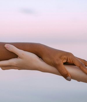deux mains qui se soutiennent l'une l'autre avec en fond un ciel de fin de journée